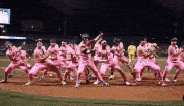 a group of baseball players in pink uniforms are dancing on a baseball field