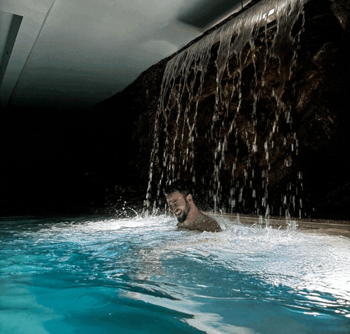 a man in a pool with a waterfall behind him