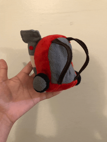 a person is holding a red and gray stuffed toy in their hand