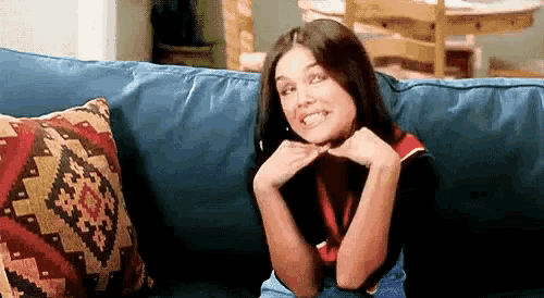 a woman is sitting on a blue couch with her hands on her chin .