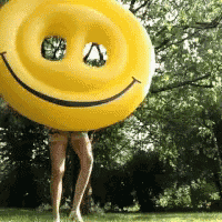 a woman is holding a yellow smiley face inflatable in front of her head