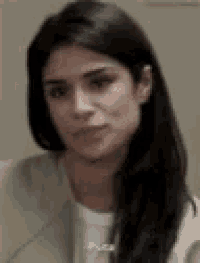 a woman with long black hair is wearing a white shirt and a brown jacket .