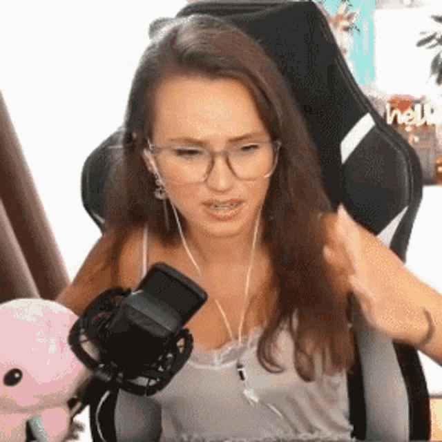 a woman wearing glasses is sitting in a chair in front of a microphone and a stuffed animal .