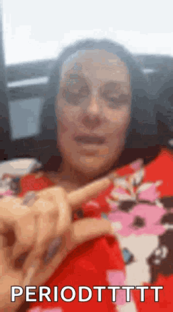 a woman in a red shirt is making a peace sign with her finger while sitting on a bed .