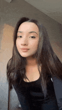 a woman with long dark hair is wearing a black top and standing in front of a wall .
