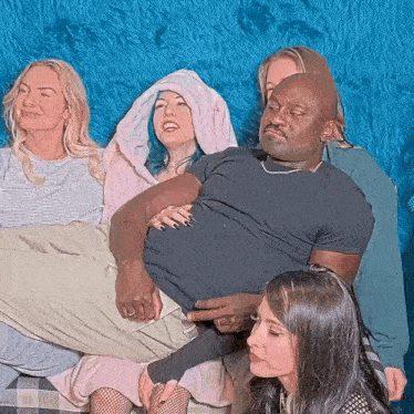 a group of women are sitting around a man laying on a bed