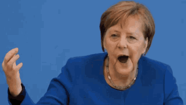 a woman wearing a blue jacket and necklace is making a funny face