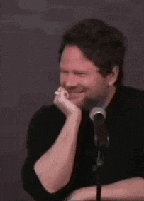 a man is sitting in front of a microphone with his hand on his chin and smiling .