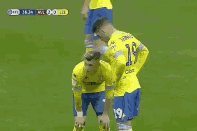 a group of soccer players are standing on a field and one of them is wearing a yellow jersey with the number 19 on it .