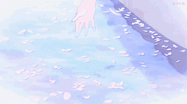 a person 's hand is touching a body of water with pink petals on the ground
