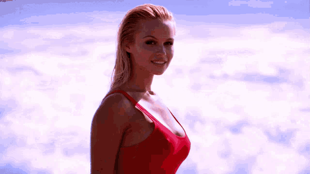 a woman in a red tank top stands in front of a cloudy sky