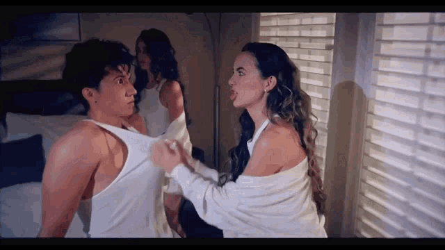a woman is holding a man 's shirt while another woman looks on