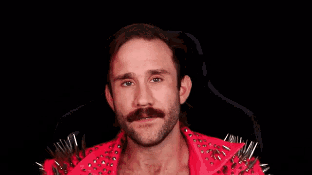 a man with a mustache is wearing a red jacket with spikes and the words think about it