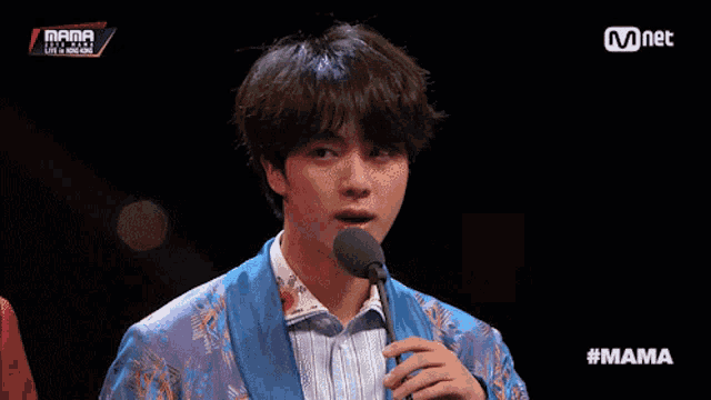 a man in a blue jacket is speaking into a microphone with mama written on the bottom