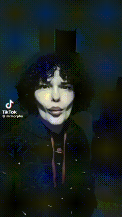 a man with curly hair is standing in front of a door with his mouth open and a tiktok video behind him