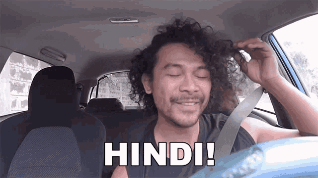 a man with curly hair is sitting in a car with the word hindi written on the back