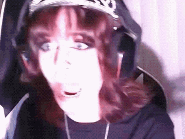 a woman wearing headphones and a hat is looking at the camera and making a funny face .