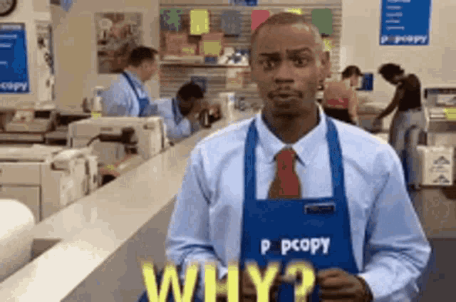 a man wearing an apron that says why is standing in front of a counter in a store