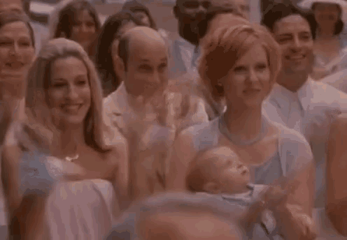 a woman is holding a baby in her arms while sitting in a crowd of people .