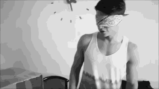 a man wearing a bandana around his eyes is standing in front of a clock