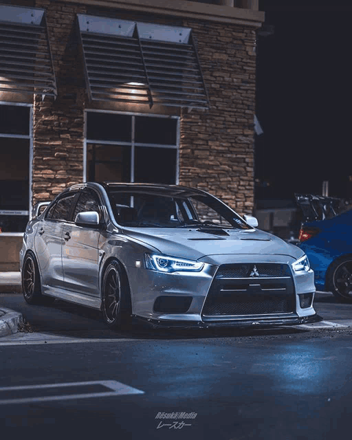 a silver mitsubishi lancer is parked in front of a stone building at night