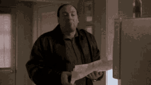a man in a brown jacket is holding a piece of paper in his hand .
