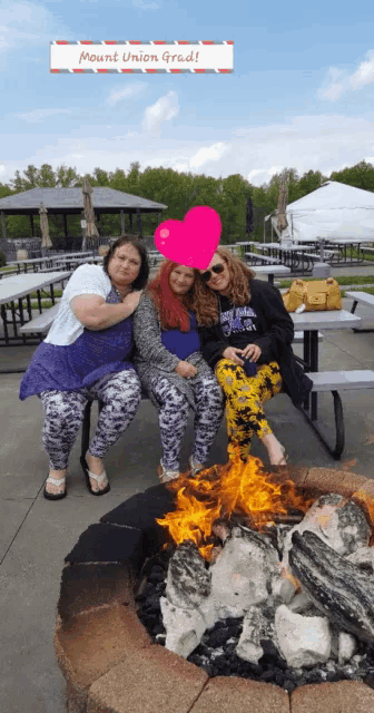 three women are sitting around a fire pit with a sign above them that says mount union grad