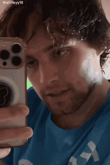 a man in a blue shirt is taking a picture of himself with his phone .