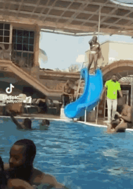 a woman in a bikini is standing on top of a blue water slide in a swimming pool .