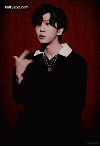 a young man wearing a black shirt and a necklace is standing in front of a red curtain