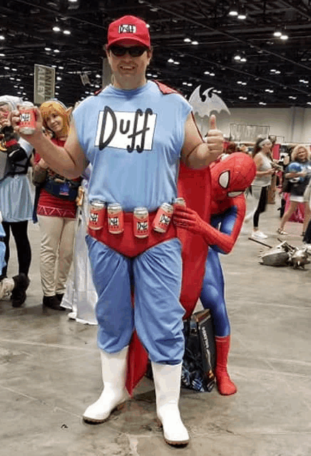 a man in a duff shirt is standing next to a spiderman costume
