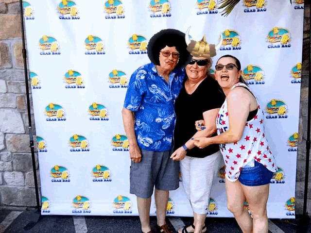 three people pose for a picture in front of a crab bag backdrop