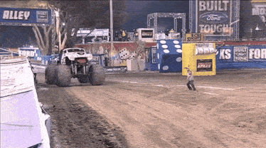 a monster truck is driving down a dirt road in front of a sign that says alley