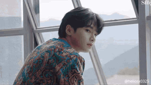 a young man is sitting in front of a window looking out .