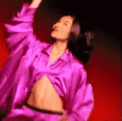 a woman in a purple shirt is dancing with her arms outstretched
