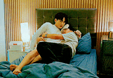 two men are hugging each other on a bed in a room