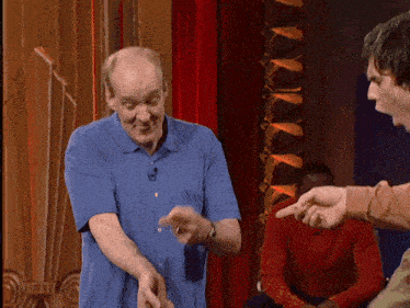 a man in a blue shirt is standing in front of a red curtain