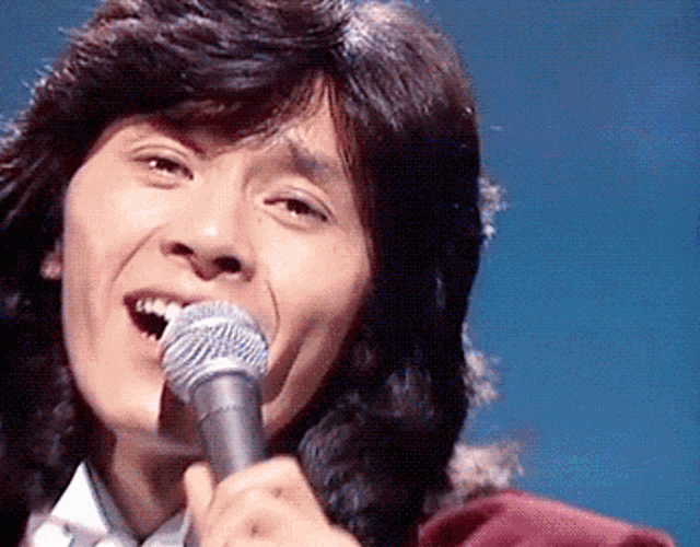 a man singing into a silver microphone with his mouth open