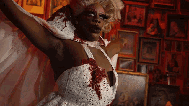 a woman in a white dress with blood coming out of it stands in front of a wall of framed pictures