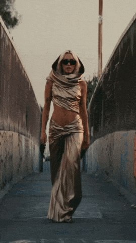 a woman in a gold dress and sunglasses is walking down a street
