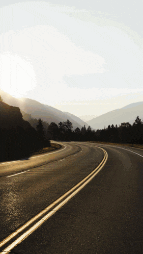 a road with mountains in the background and the sun shining on it