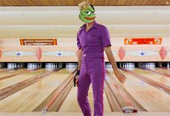 a man in purple pants with a green frog head on his head stands in a bowling alley