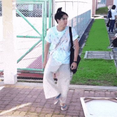 a man is walking down a sidewalk with a bag on his shoulder .
