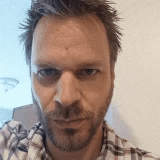 a man with a beard and plaid shirt looks at the camera