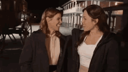 two women are standing next to each other and laughing .