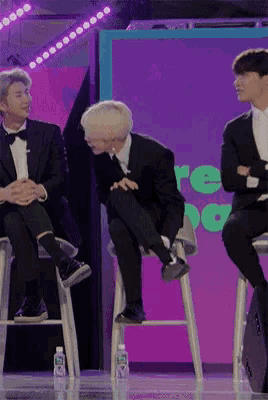 three men in suits sit on stools in front of a sign that says " re "