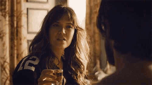 a woman is holding a glass of whiskey and looking at a man .