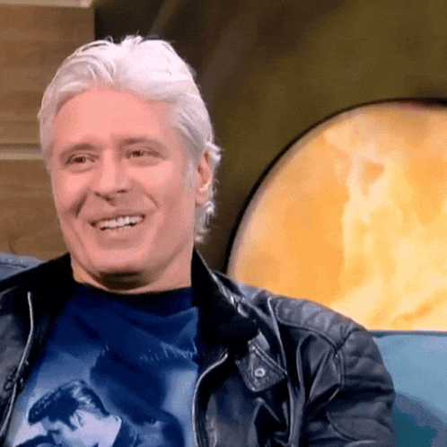 a man wearing a leather jacket and a blue shirt smiles for the camera