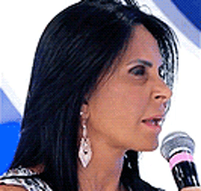a woman is speaking into a microphone while wearing earrings and a shirt .