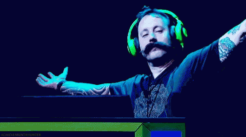 a man with a mustache wearing green headphones stands in front of a computer